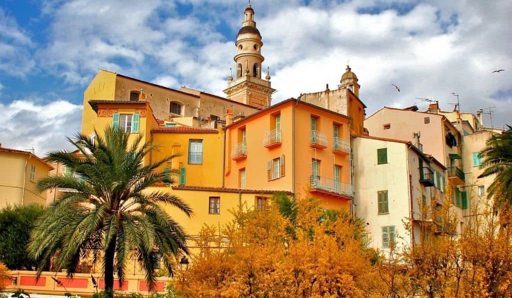 Gorgeous, colorful buildings under a cloudy sky with palm trees in Menton's Old Town.
