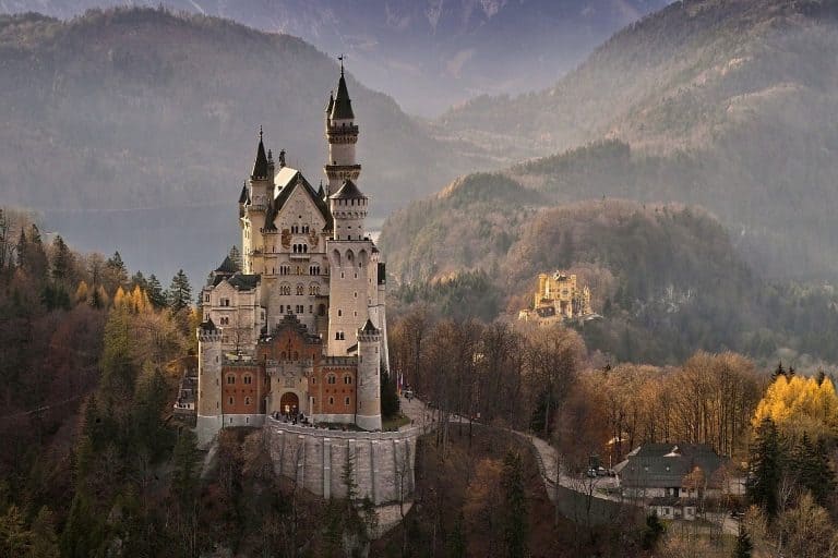 Dreamy Neuschwanstein Castle in Germany, seen from afar with autumn trees in the background.