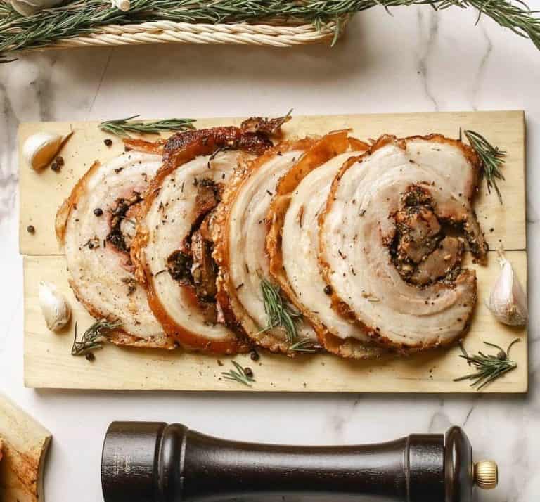 Slices of porchetta surrounded by chopped rosemary and garlic cloves
