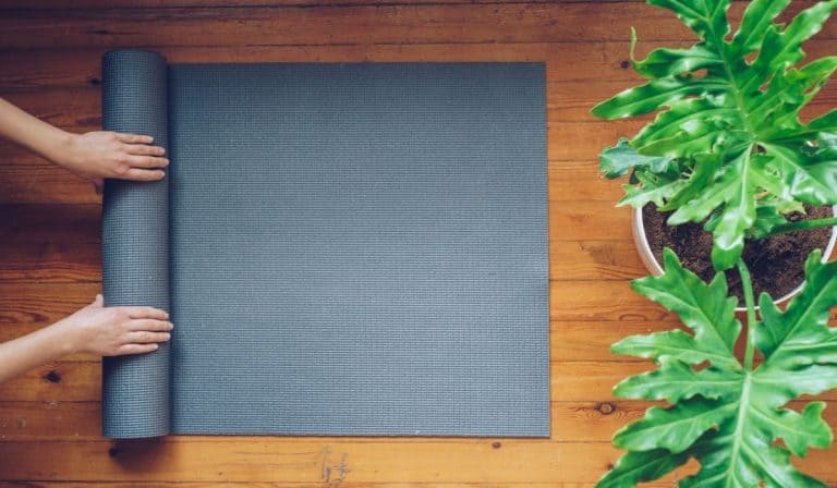 Hands rolling up a yoga mat next to large green, leafy plants.